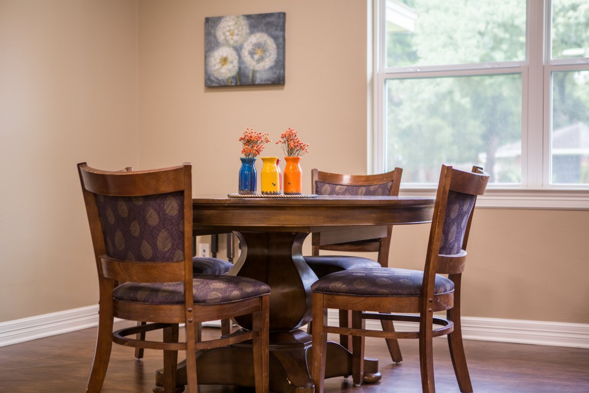 A cozy dining area with a wooden table, surrounded by four chairs and decorated with colorful vases of flowers.