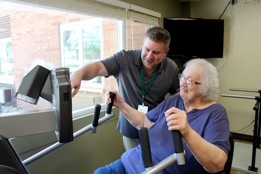 A trainer assists an elderly woman during a fitness session, focusing on rehabilitation and exercise.