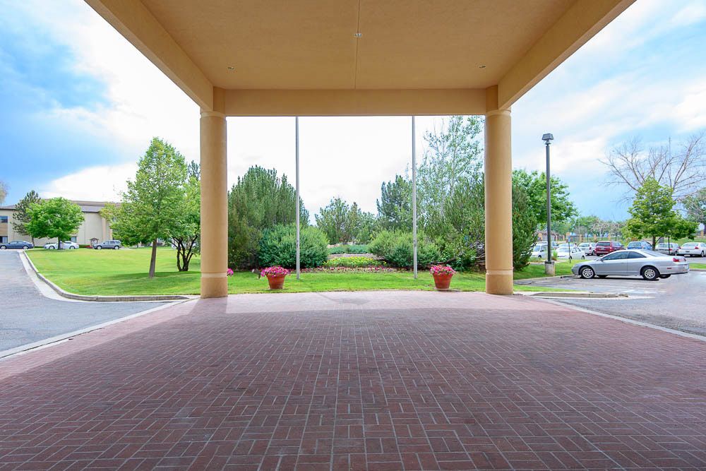 A covered walkway with brick flooring opens to a scenic outdoor view with trees and planters.