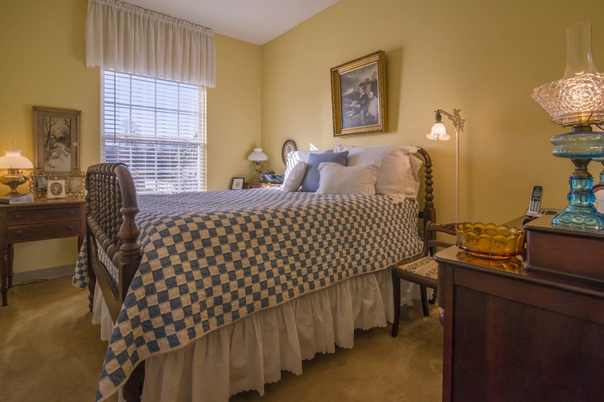 A cozy bedroom featuring a neatly made bed with patterned bedding, soft lighting, and traditional decor elements.