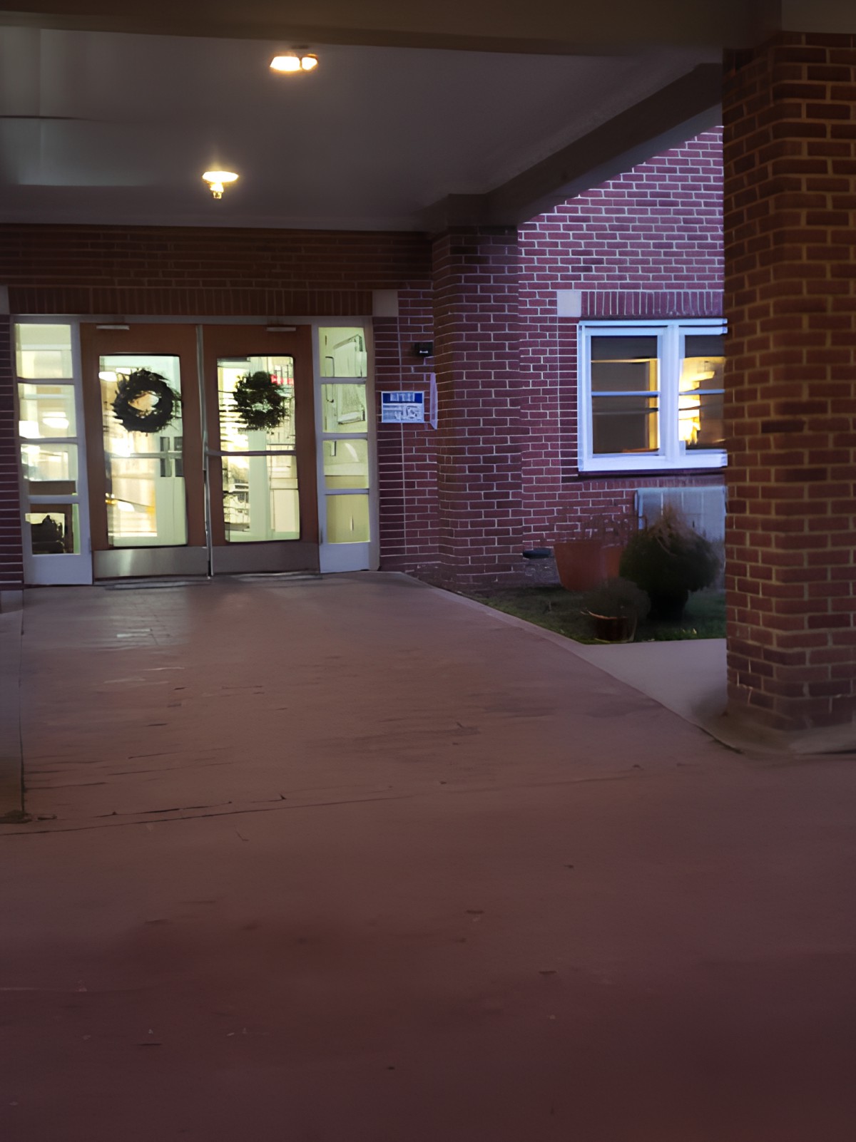A building entrance at night adorned with wreath decorations on the doors.