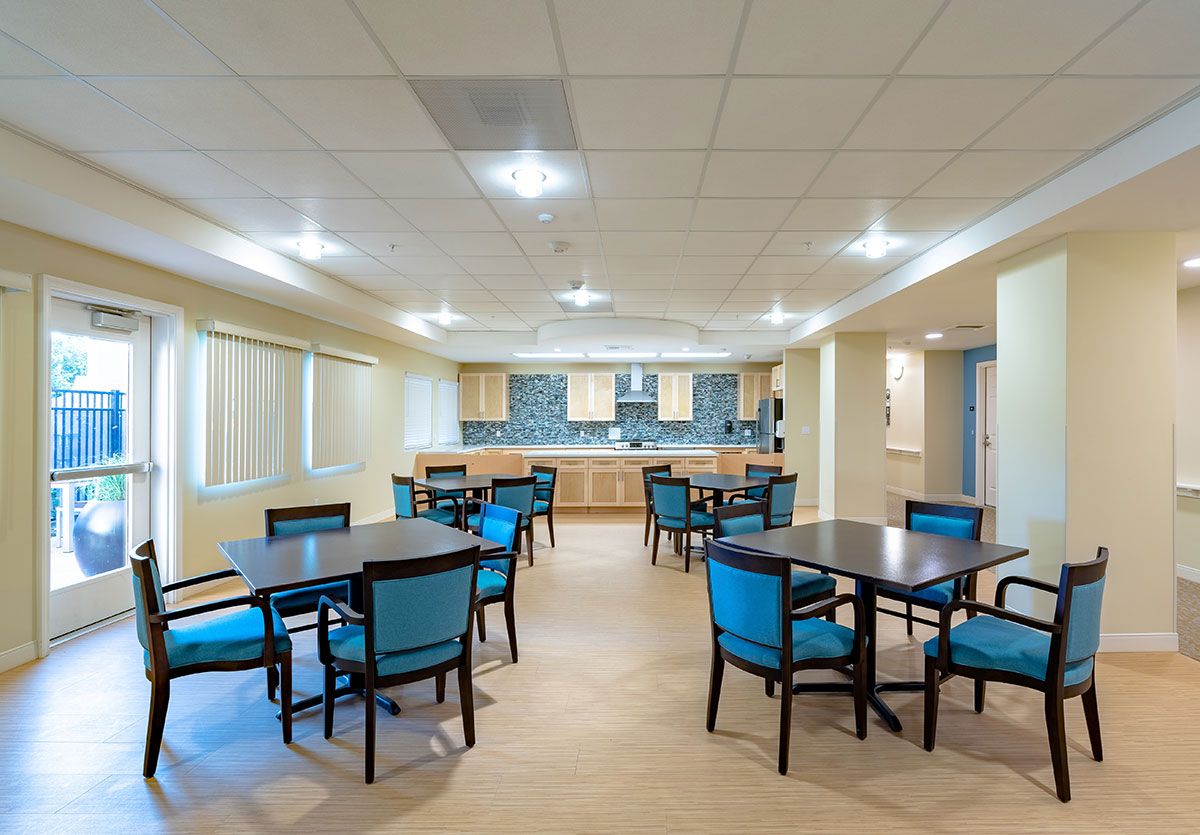 A spacious dining area with multiple tables and chairs, featuring an adjacent kitchen.