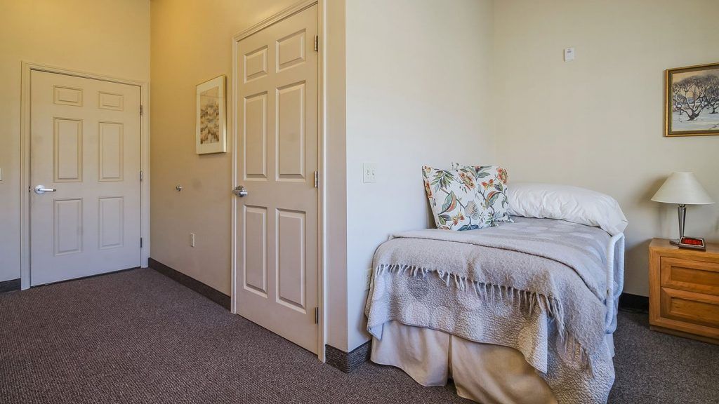 A cozy bedroom with a neatly made bed and decorative pillows beside a closed door.