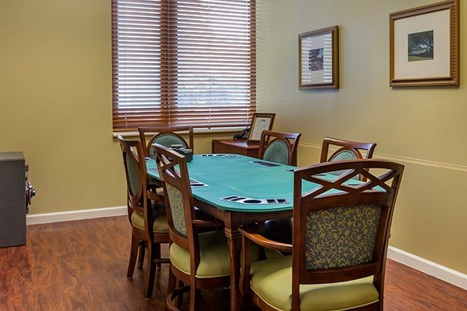 A room with a poker table surrounded by chairs, featuring wooden blinds and a framed picture on the wall.