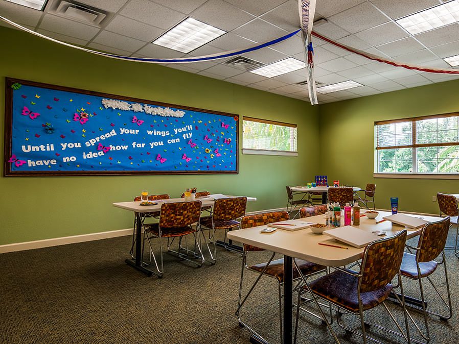 A decorated classroom with tables and chairs, featuring a bulletin board and windows.