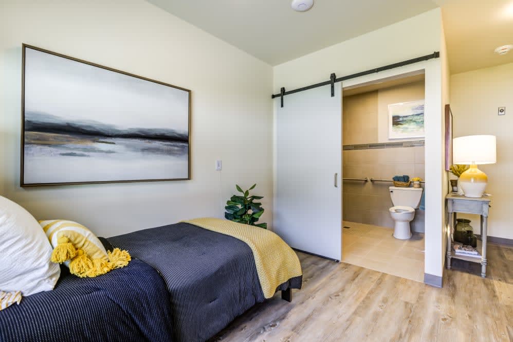 A modern and minimalist bedroom featuring a sliding door leading to an en-suite bathroom.