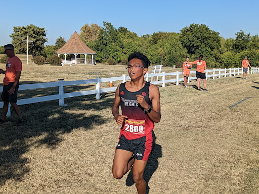 A young athlete competing in a cross country race on a sunny day.