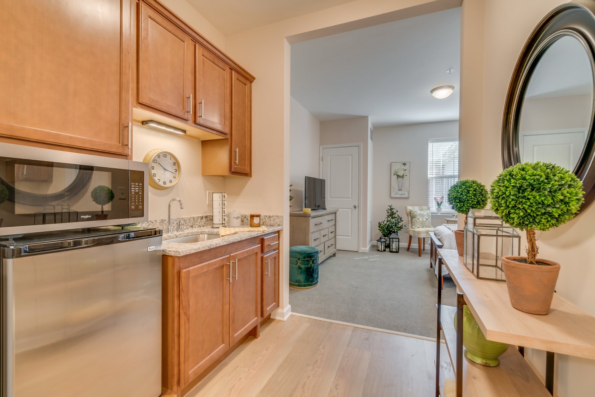A modern apartment kitchen with wooden cabinets leading into a cozy living area.