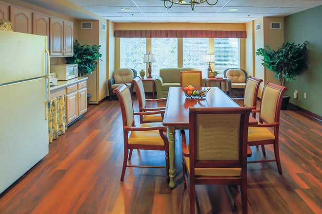 A cozy dining area with a large table, surrounded by chairs and natural light from large windows.