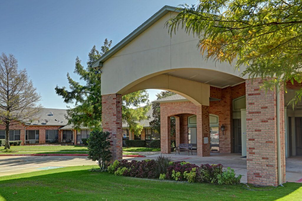A well-maintained building entrance with brick columns and lush landscaping.