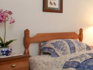 A cozy bedroom with a wooden headboard bed, floral quilt, and side table with a lamp.