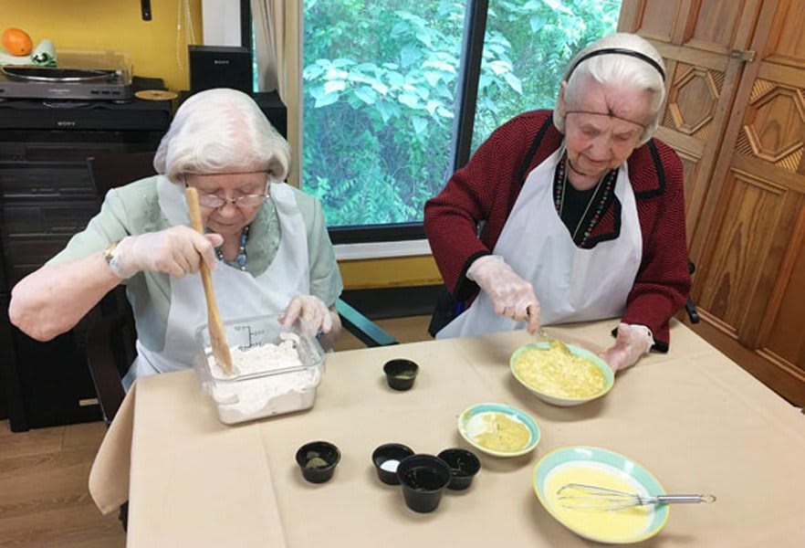 Two elderly women engaged in a cooking activity, preparing ingredients at a table.