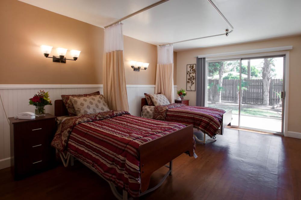 A warmly lit shared room in a nursing home featuring two beds separated by curtains.