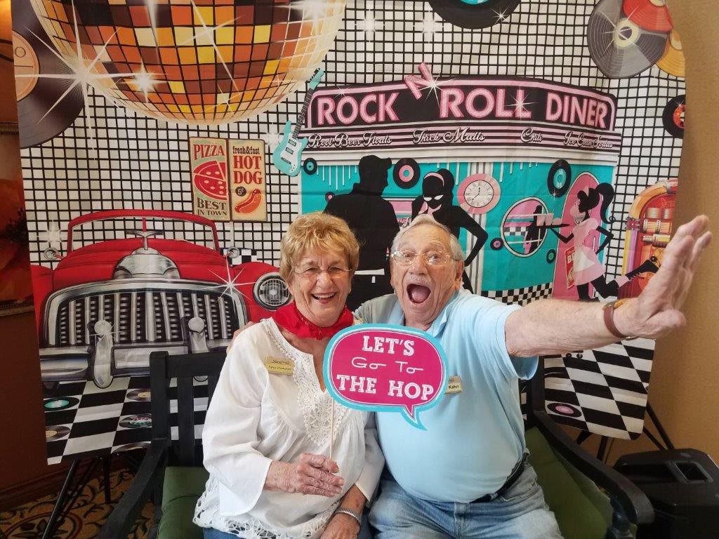 A joyful couple posing with props at a retro-themed rock and roll diner setting.