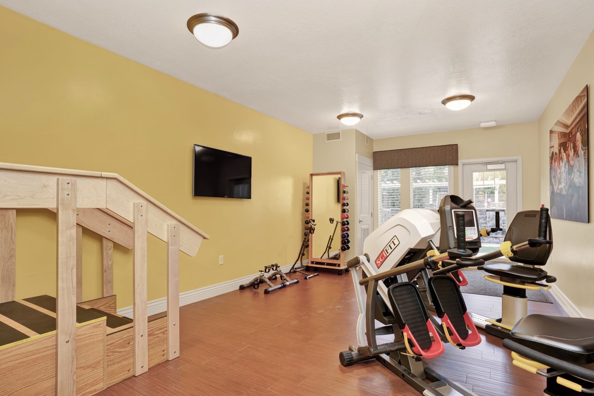A modern gym with various exercise equipment and a TV on the wall.
