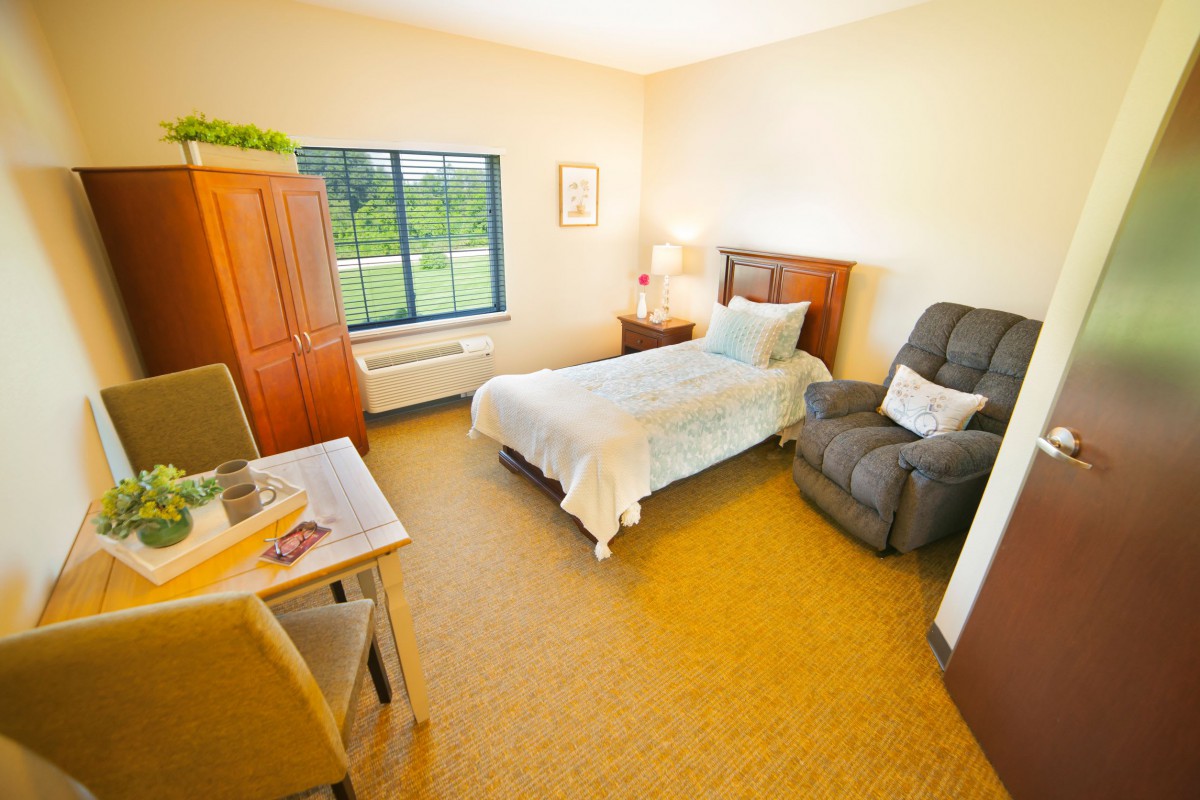 A cozy bedroom with a single bed, armchair, and large window.