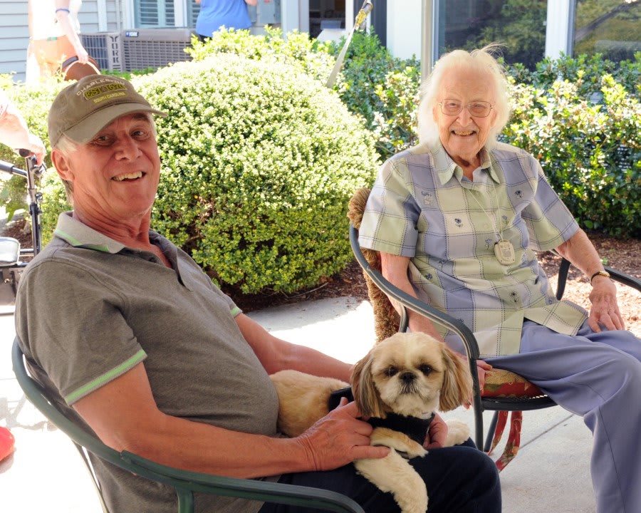 Two people sitting outdoors with a dog on a sunny day.