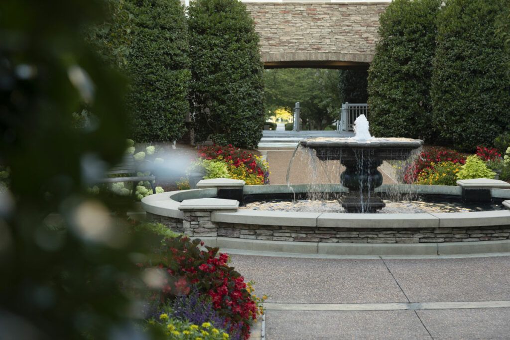 A garden with a central fountain surrounded by trees and flowers.