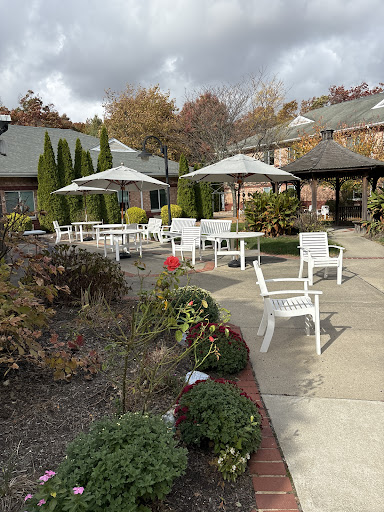 A serene outdoor patio area featuring white chairs and umbrellas surrounded by seasonal foliage.