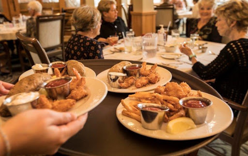 A server delivers plates of fried seafood to a dining table in a restaurant.