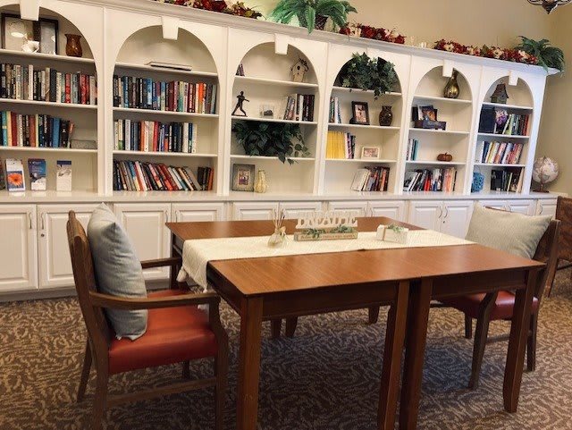 A cozy reading area with a wooden table, chairs, and a large bookshelf in the background.