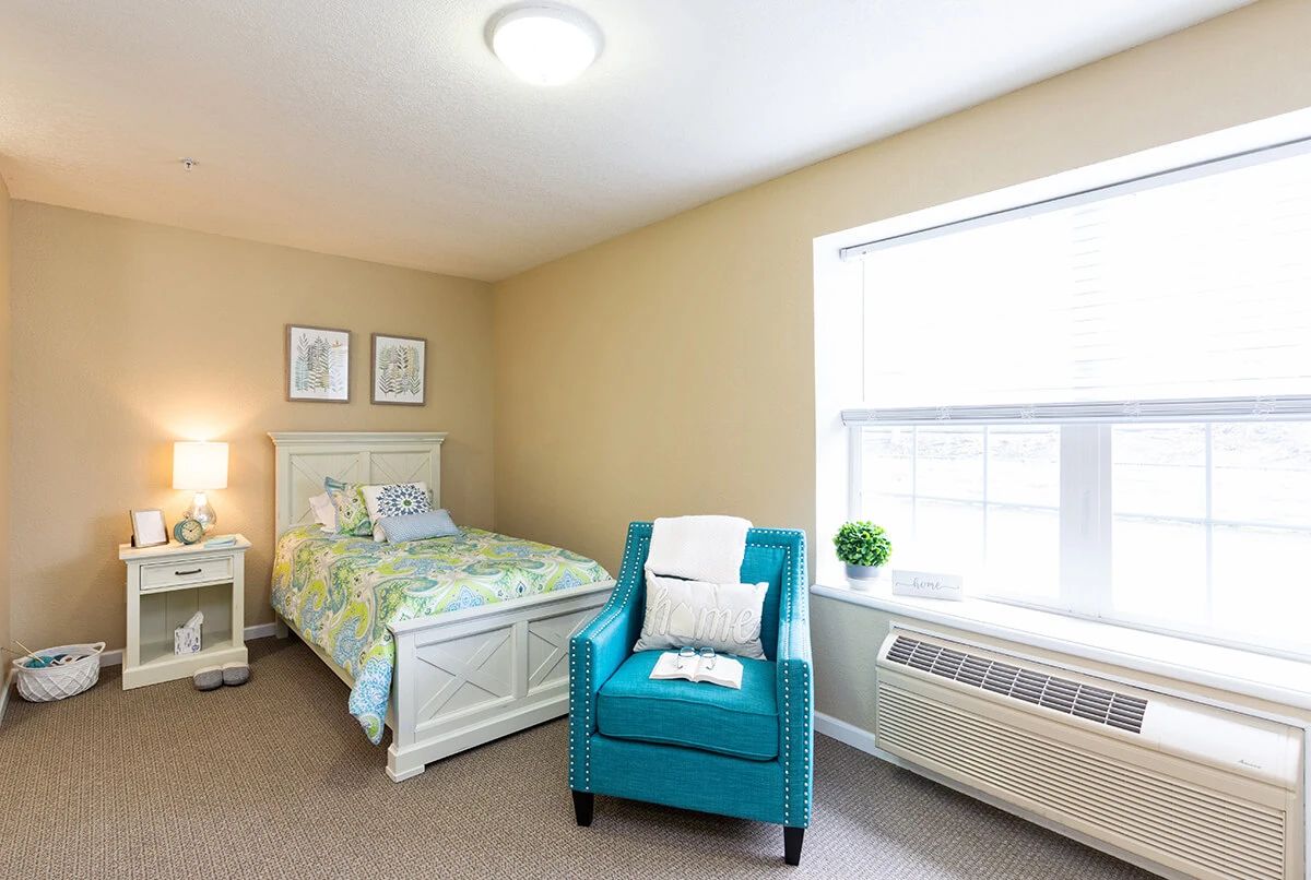 A cozy bedroom with a single bed and a turquoise armchair near a window.