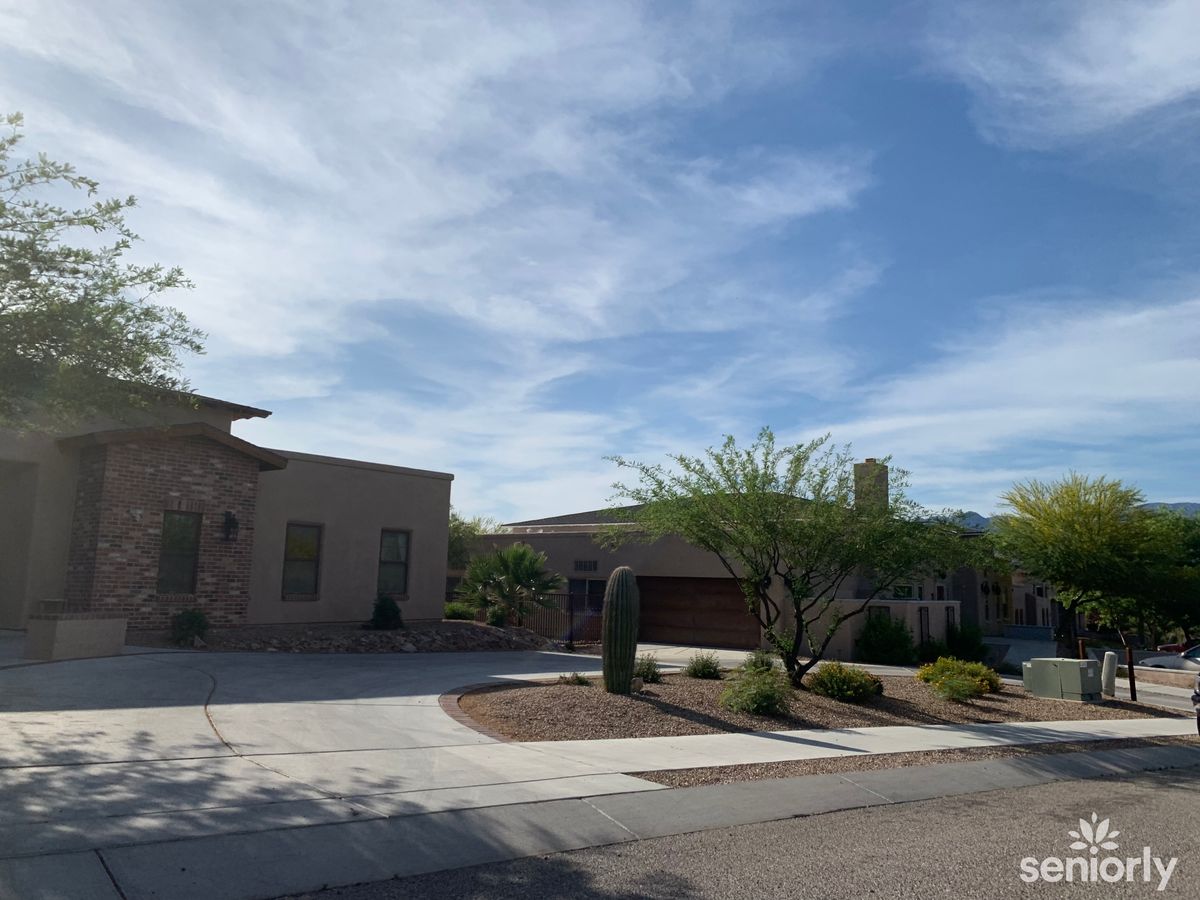 A suburban house set in a desert landscape with a driveway and trees under a cloudy sky.
