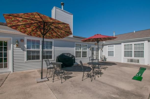 A sunny patio with tables, chairs, and umbrellas outside a house.
