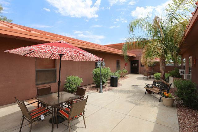 A sunny courtyard with outdoor seating and patio umbrellas, surrounded by a building and palm trees.