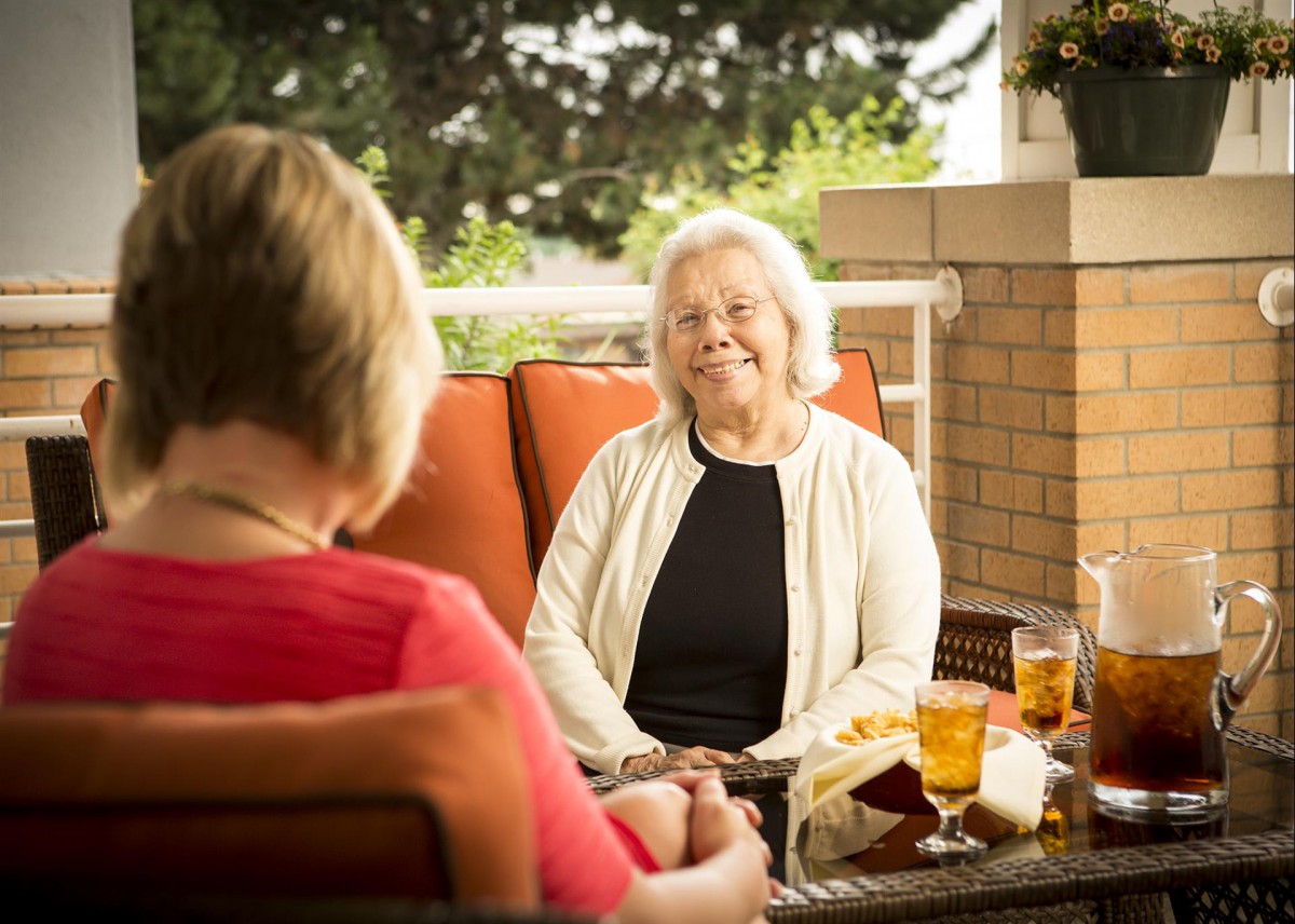 Two elderly women enjoying a conversation on a sunny patio.