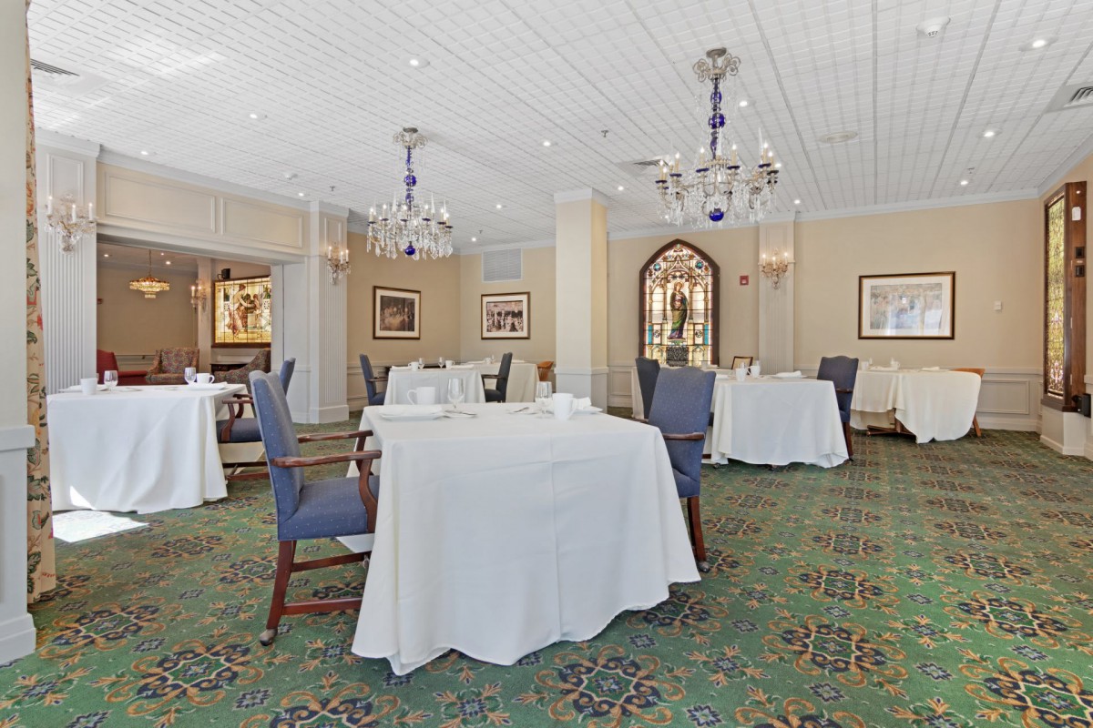 A spacious dining area with elegantly set tables, comfortable chairs, and decorative chandeliers.