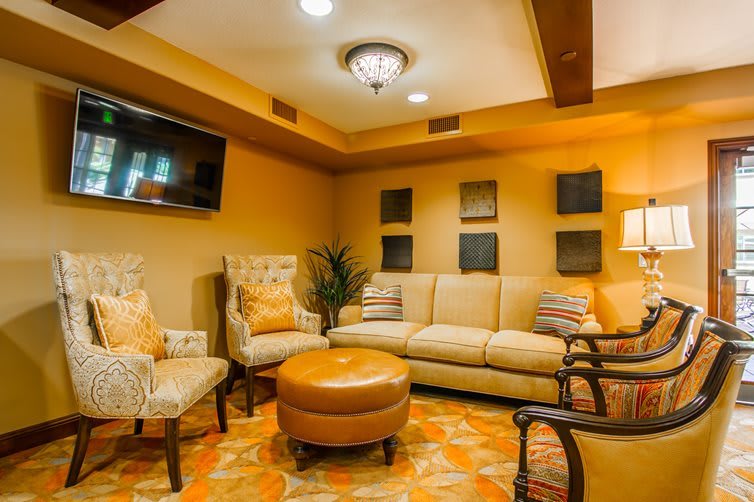 A cozy living room with a comfortable sofa, armchairs, and an ottoman, complemented by warm lighting and decorative wall art.