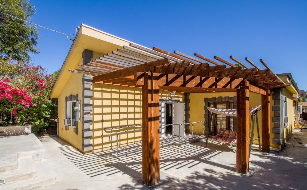 A modern house with yellow walls and a wooden pergola in a sunny outdoor setting.