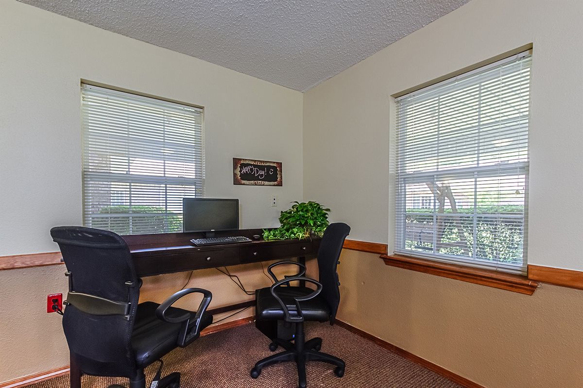 A small office space with a desk, computer, and chairs by two large windows.