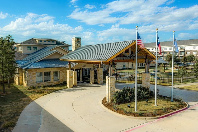 A building with a covered entrance and flags displayed in front, set against a partially cloudy sky.