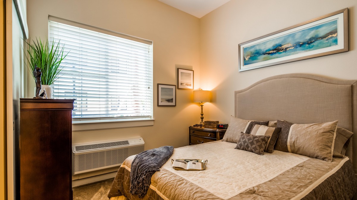 A cozy bedroom with a neatly made bed, warm lighting from a lamp, and wall art.
