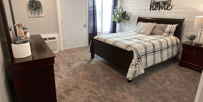 A cozy bedroom with a neatly made bed, carpeted floor, and soft lighting.