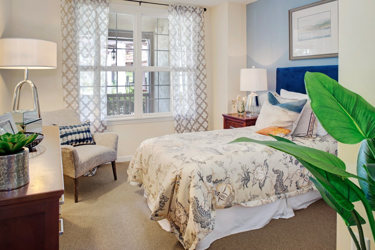A cozy bedroom with a neatly made bed, soft lighting, and a large window letting in natural light.