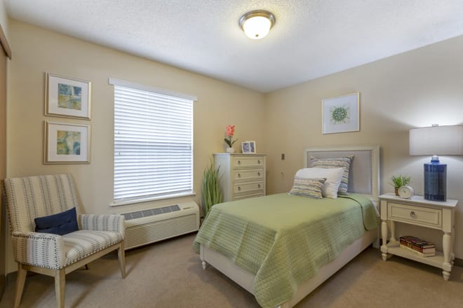 A cozy bedroom with a single bed featuring green bedding and simple, elegant decor.