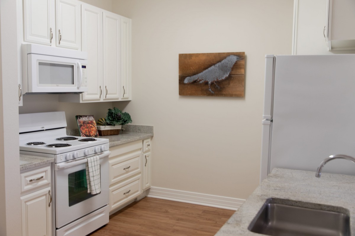 A cozy kitchen featuring white appliances and cabinets with a piece of artwork on the wall.