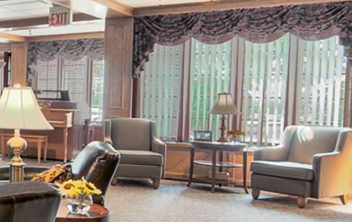 A comfortable lounge area with two armchairs, a side table, and a lamp in front of large windows adorned with curtains.