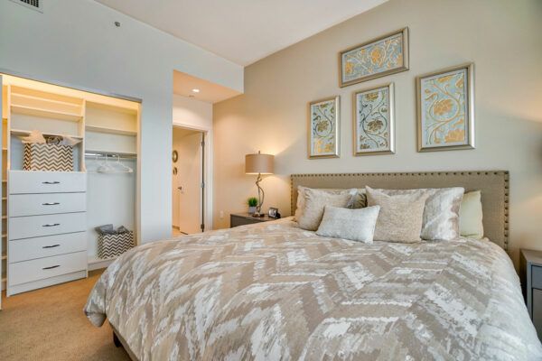 A well-decorated bedroom with neutral tones, featuring a comfortable bed, stylish lamp, and framed artwork on the wall.