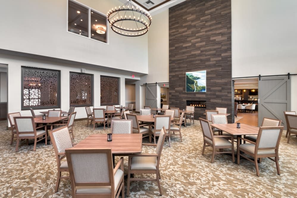 A modern dining area with neatly arranged tables and chairs, featuring a large chandelier and a central fireplace.