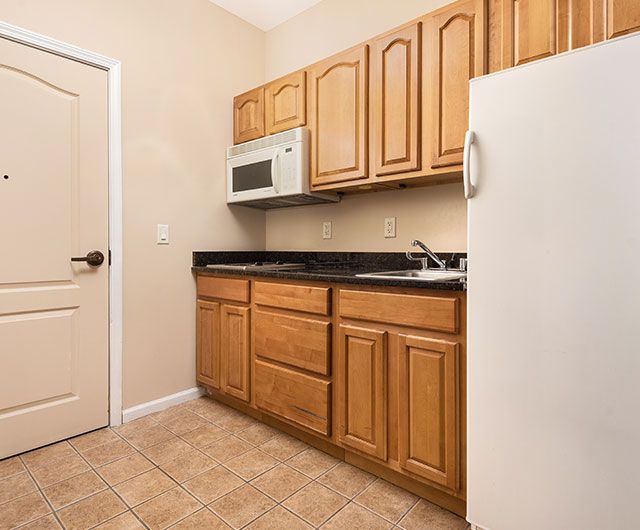 A compact kitchen with wooden cabinets, a microwave, refrigerator, and a sink.