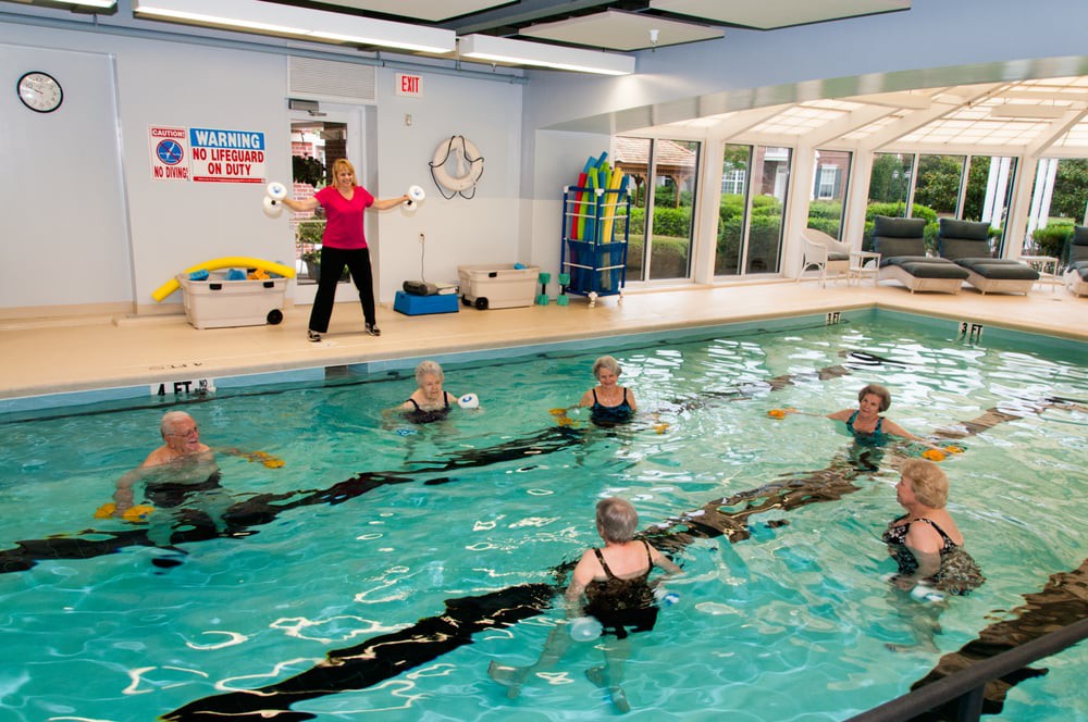 A group of seniors participating in an aquatic exercise class led by an instructor in an indoor swimming pool.