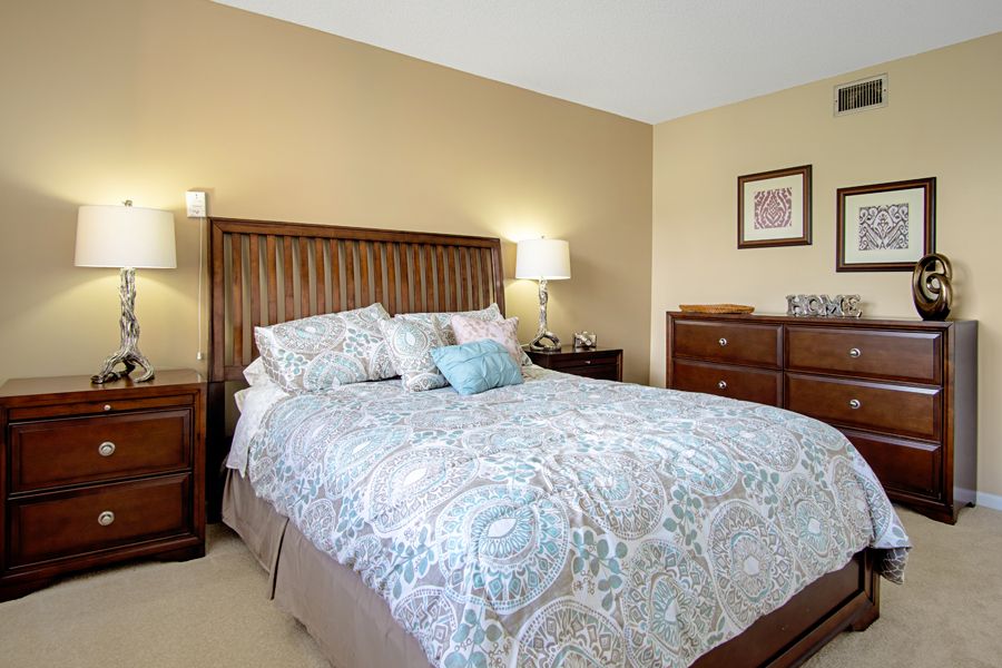 A cozy bedroom featuring a neatly made bed with patterned bedding, bedside tables with lamps, and a dresser.