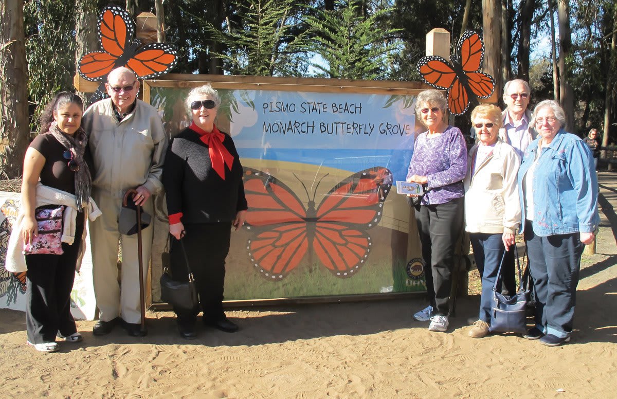 A group of people standing in front of a butterfly sanctuary sign outdoors.