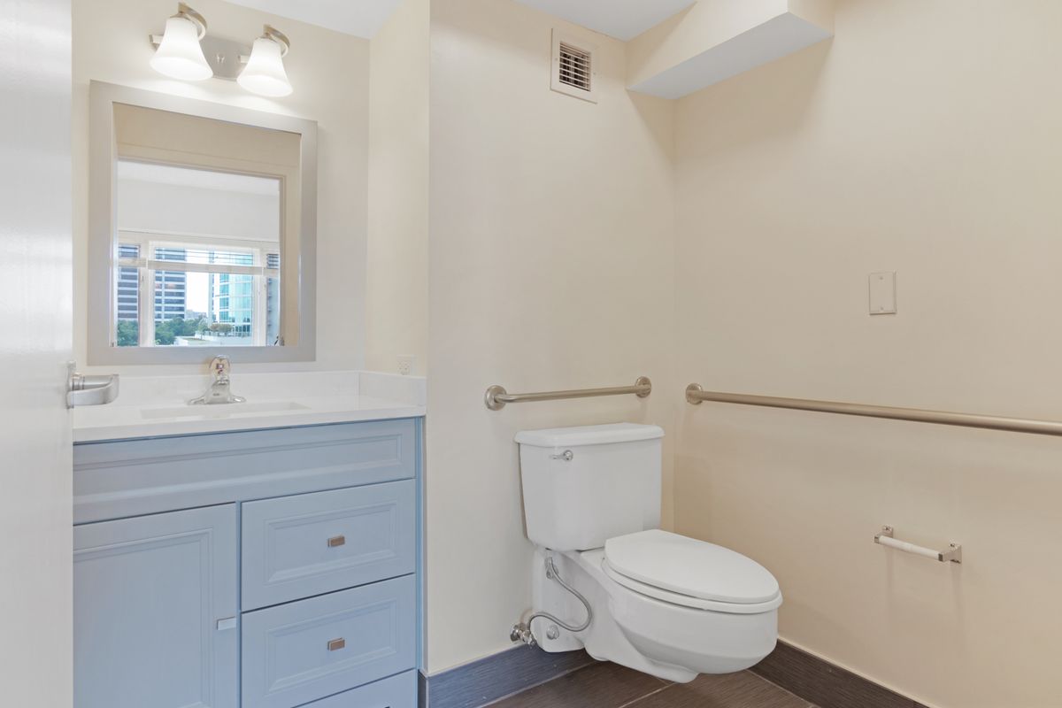 A clean and accessible bathroom with a toilet, vanity, and handrails.