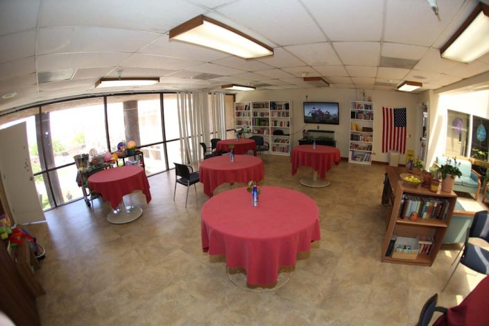 A spacious indoor event area featuring tables with red tablecloths, chairs, a flag, and a television.