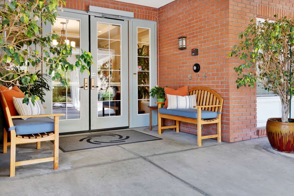 A welcoming entrance with a wooden bench and greenery beside glass double doors.